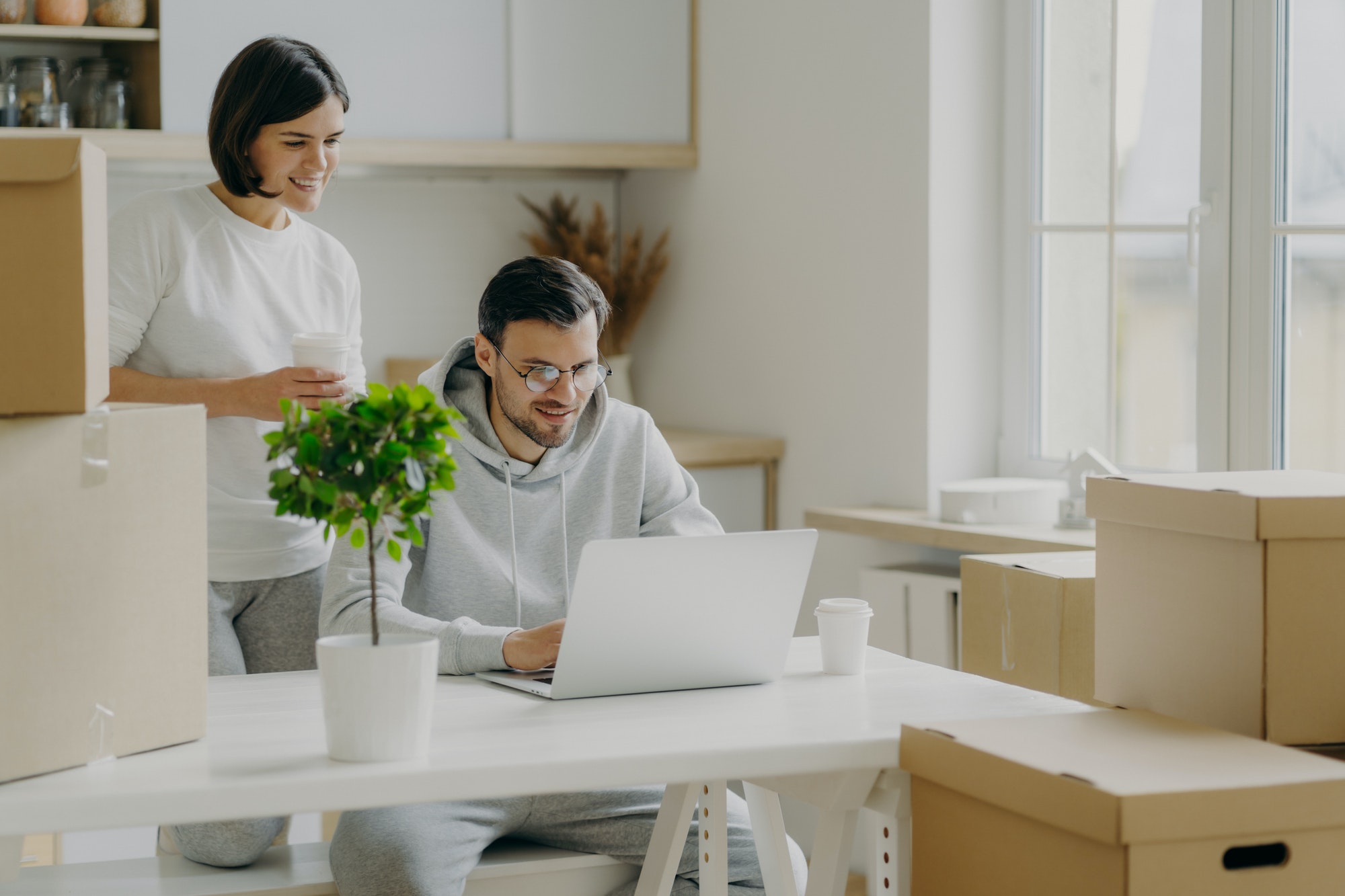 Happy woman and man spend morning at their new kitchen with big windows and modern furniture